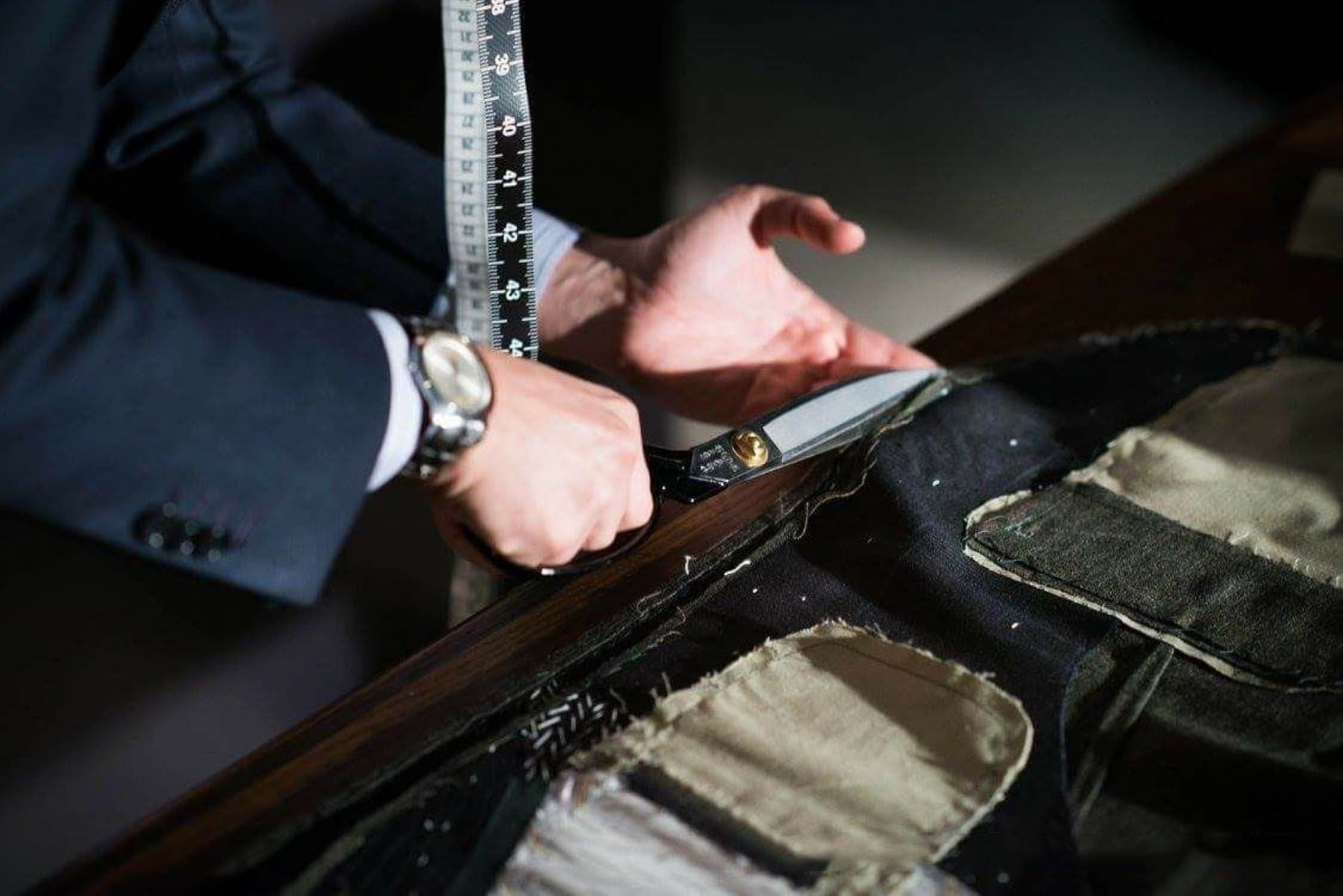 Tailor cutting suit fabric with shears, tape measure and canvas pieces on the table